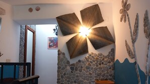 Een kamer met een stenen muur, een grote bloemvormige lamp, een rustieke vaas en een ingelijst kunstwerk.