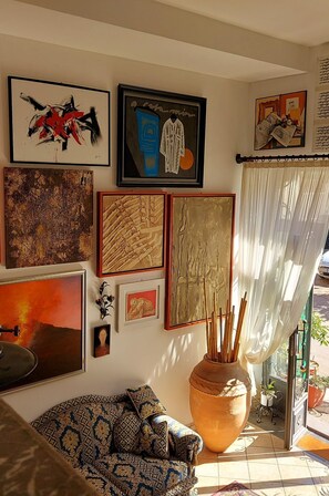 A living room with a patterned sofa, a large vase with sticks, and various framed artworks on the wall. - Sole Mare Giardini Naxos Room 'Vista' with Balcony, Wi-Fi and Air Conditioning (Giardini Naxos)
