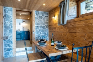 Une table à manger en bois, des murs en pierre, une bouteille et des bols.