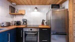 A kitchen with a stainless steel refrigerator, oven, and toaster. There is a wooden shelf with bottles and a kettle. - Apartment 'La Bergerie' with Mountain View, Private Terrace and Wi-Fi (La Giettaz)