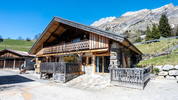 A wooden chalet with a balcony, stone foundation, and a mountain backdrop. - Apartment 'La Bergerie' with Mountain View, Private Terrace and Wi-Fi (La Giettaz)