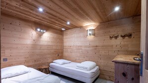 A wooden-paneled room with two beds, a small stool, a cabinet, and wall-mounted lights. - Apartment 'La Bergerie' with Mountain View, Private Terrace and Wi-Fi (La Giettaz)