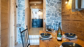 A wooden interior with stone walls, a dining table set with plates, bowls, wine glasses, and a bottle. - Apartment 'La Bergerie' with Mountain View, Private Terrace and Wi-Fi (La Giettaz)