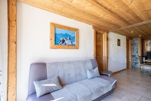 A wooden ceiling, a sofa with cushions, a framed picture of mountains, and a stone wall. - Apartment 'La Bergerie' with Mountain View, Private Terrace and Wi-Fi (La Giettaz)