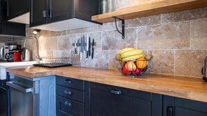 Une cuisine avec des meubles de couleur sombre, un plan de travail en bois, un panier de fruits et un porte-couteaux.