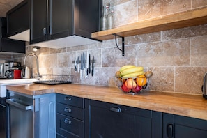 Een keuken met donkere kastjes, een houten aanrecht, een fruitschaal en een messenrek.