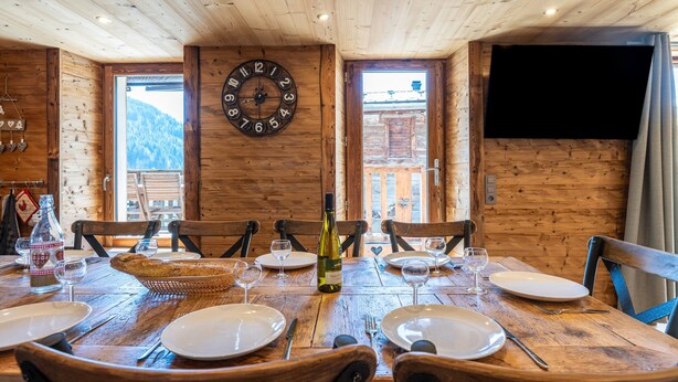Une table de salle à manger en bois, mise pour quatre personnes, avec des assiettes, des verres et une bouteille de vin.