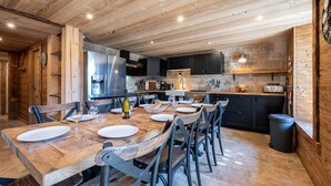 Une cuisine rustique avec des poutres en bois, une grande table à manger dressée pour six personnes et des appareils électroménagers modernes.