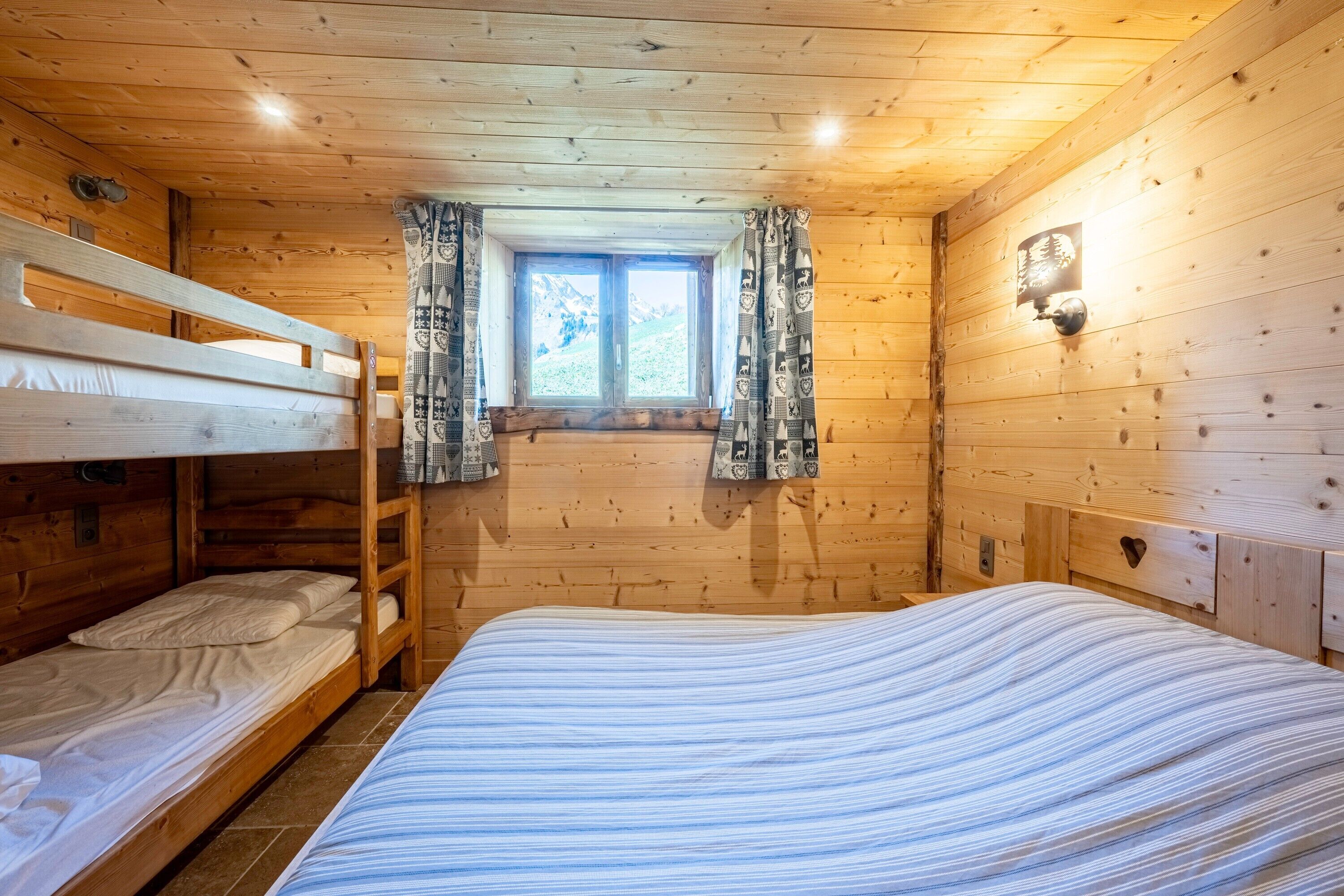 Een houten kamer met stapelbedden, een raam met gordijnen en een wandlamp.
