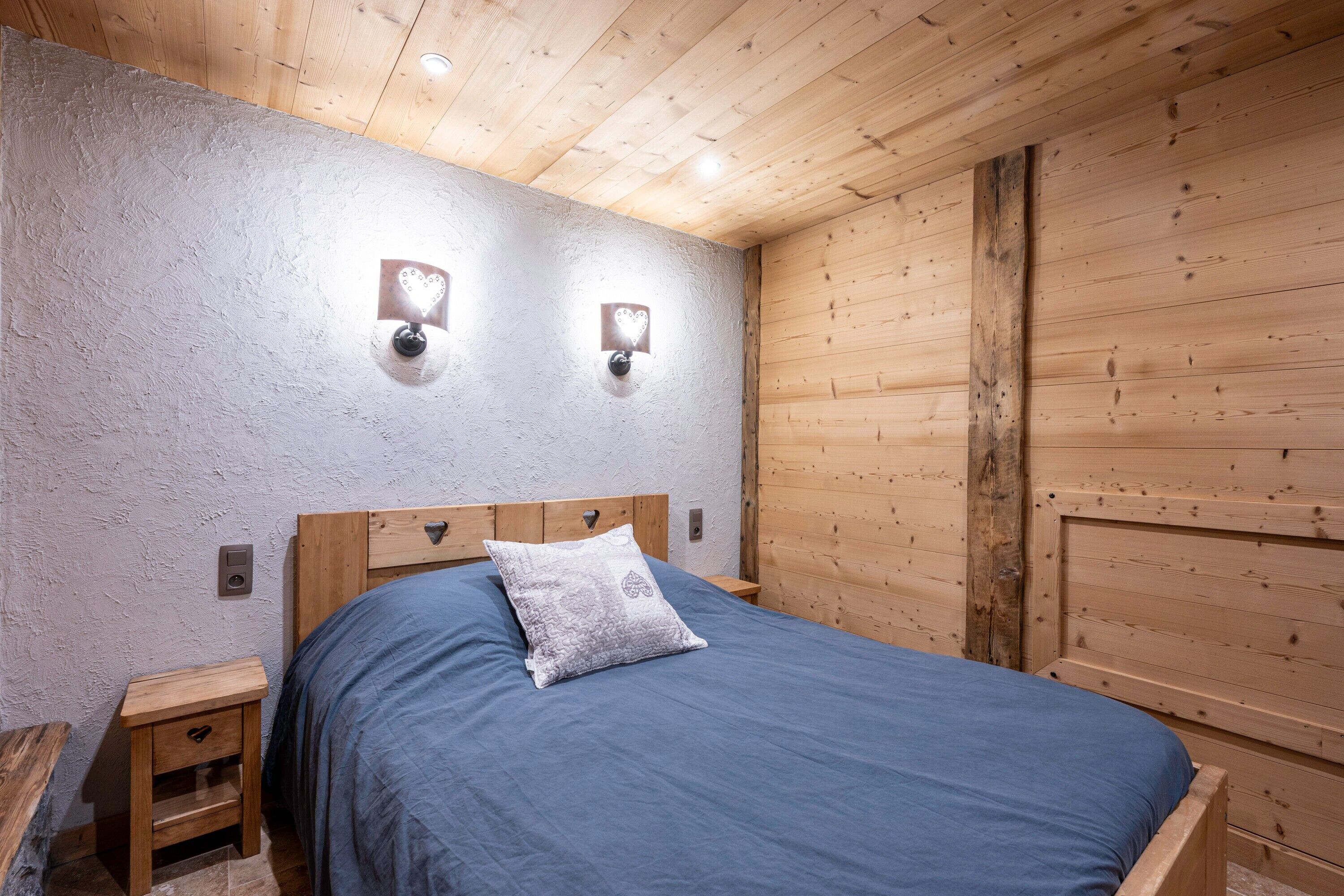 Une chambre à coucher avec une tête de lit en bois, une couvre-lit bleue, une table de chevet et deux appliques murales.