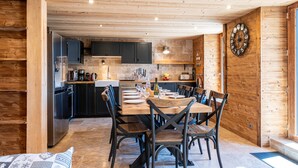 Un intérieur en bois comprenant une table à manger pour quatre personnes, des meubles de cuisine et une horloge murale.