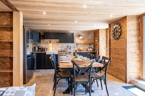 Een houten interieur met een eettafel gedekt voor vier personen, keukenkastjes en een wandklok.