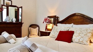 Un letto rifatto con cura, asciugamani arrotolati, una testiera in legno, un comodino con una lampada e uno specchio.