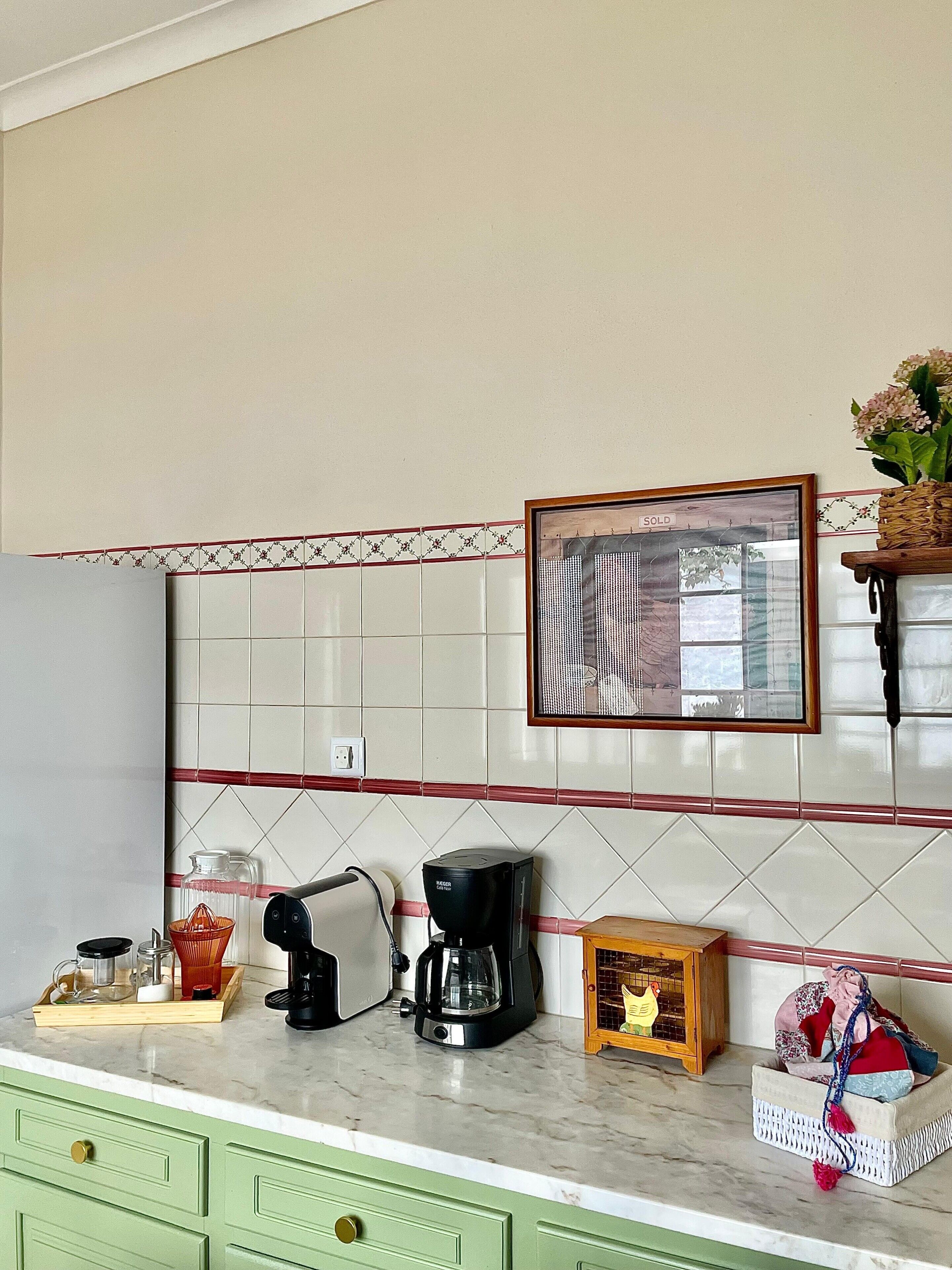 A kitchen with a tiled backsplash, a coffee maker, a basket of fruits, and a small wooden box.