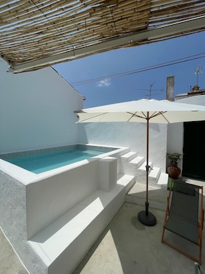 Ein Pool auf dem Dach mit weißer Fassade, einer Pergola darüber und einem Blumentopf in der Nähe.