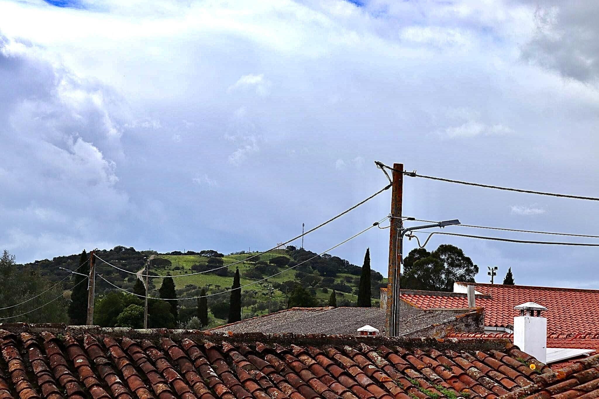 A building with a red-tiled roof, a utility pole, and a hilly landscape in the background.