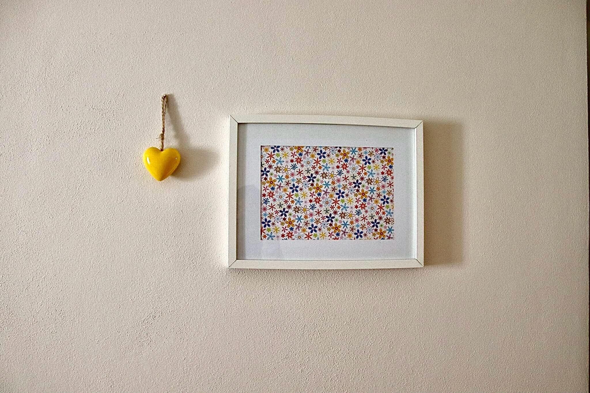 Ein gerahmtes Kunstwerk mit einem farbenfrohen Blumenmuster an einer strukturierten Wand.