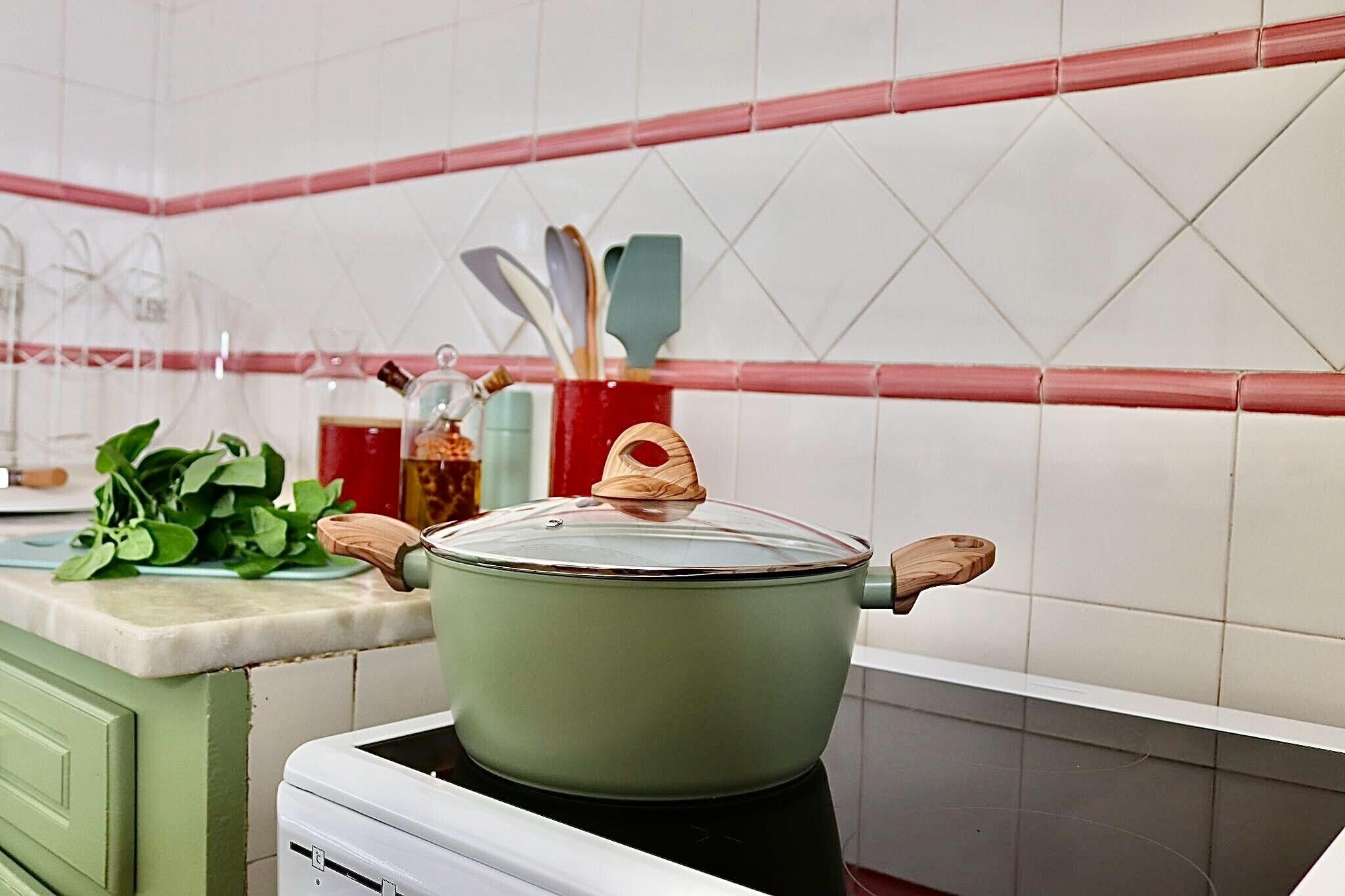 A kitchen with a green pot on the stove, a red container with utensils, and a green plant on the counter.