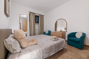 Una camera da letto con un letto, una sedia, una cassettiera, uno specchio e una finestra con tende.