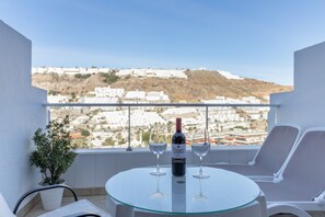 Een balkon met een tafel, twee glazen, een fles wijn en een bloempot.