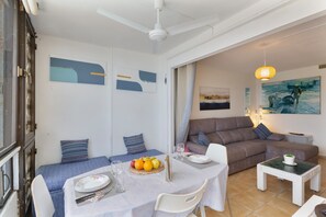 A dining area with a table set for two, a sofa, and a small table with a plant.