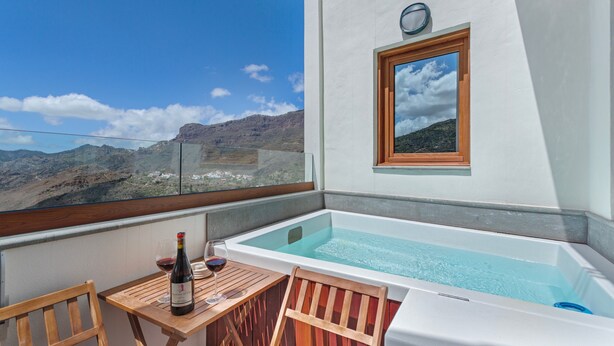 A balcony with a hot tub, a table with a bottle of wine, and a chair.