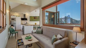A modern living room with a sofa, a dining table, and a view of a mountain.