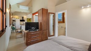A bedroom with a bed, wooden dresser, and a view of the kitchen.