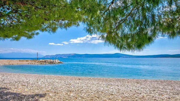 Une plage de galets bordée d’une eau d’un bleu limpide et dominée par des montagnes lointaines.