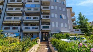 Un immeuble résidentiel à plusieurs étages, doté de balcons, d’un chemin pavé et d’une voiture garée devant.
