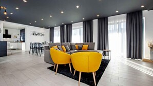Un salon moderne avec un canapé gris, des fauteuils jaunes et un coin repas à l’arrière-plan.
