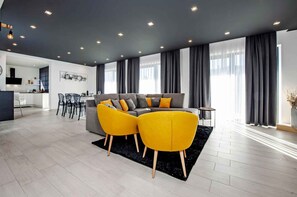 Een moderne woonkamer met een grijze bank, gele fauteuils en een eethoek op de achtergrond.