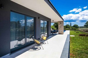 Een modern huis met een patio, glazen deuren, een zwembad en buitenmeubilair.