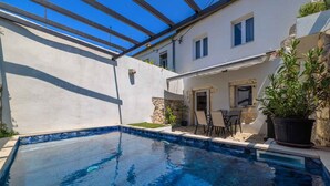 A swimming pool with a pergola overhead, a patio area with chairs, and a stone wall. - Holiday home with swimming pool and barbecue (Grižane)