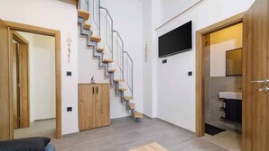A modern living room with a staircase, a flat-screen TV, and a wooden cabinet. - Holiday home with swimming pool and barbecue (Grižane)