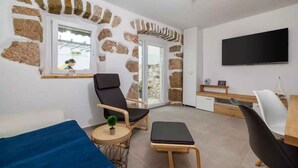 A modern living room with stone walls, a flat-screen TV, a sofa, a coffee table, and a dining area with a wooden table and chairs. - Holiday home with swimming pool and barbecue (Grižane)
