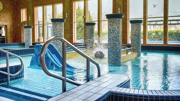 Ein Hallenbad mit Rutsche, gefliesten Wänden und großen Fenstern.