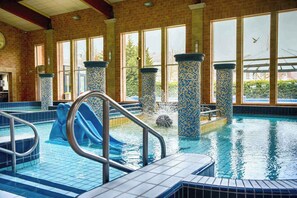 An indoor swimming pool with a slide, tiled walls, and large windows.