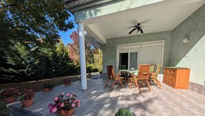 A covered patio with a table and chairs, surrounded by potted plants and a wooden cabinet. - Holiday apartment near the beach with a large terrace (Siófok)