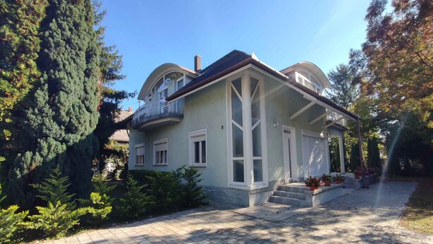 A two-story house with a balcony, a covered porch, and a paved driveway. - Holiday apartment near the beach with a large terrace (Siófok)