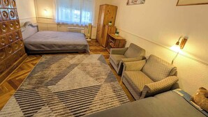 A bedroom with a bed, a sofa, a wooden wardrobe, a small table with a plant, and a wall-mounted lamp. - Holiday apartment near the beach with a large terrace (Siófok)