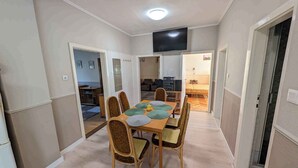 A dining area with a wooden table and chairs, a flat-screen TV mounted on the wall, and a small kitchenette in the background. - Holiday apartment near the beach with a large terrace (Siófok)