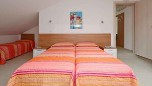 A bedroom with two beds, a wooden headboard, a painting on the wall, and a door to the right. - Holiday apartment with air conditioning, internet, balcony and pool (Lignano)