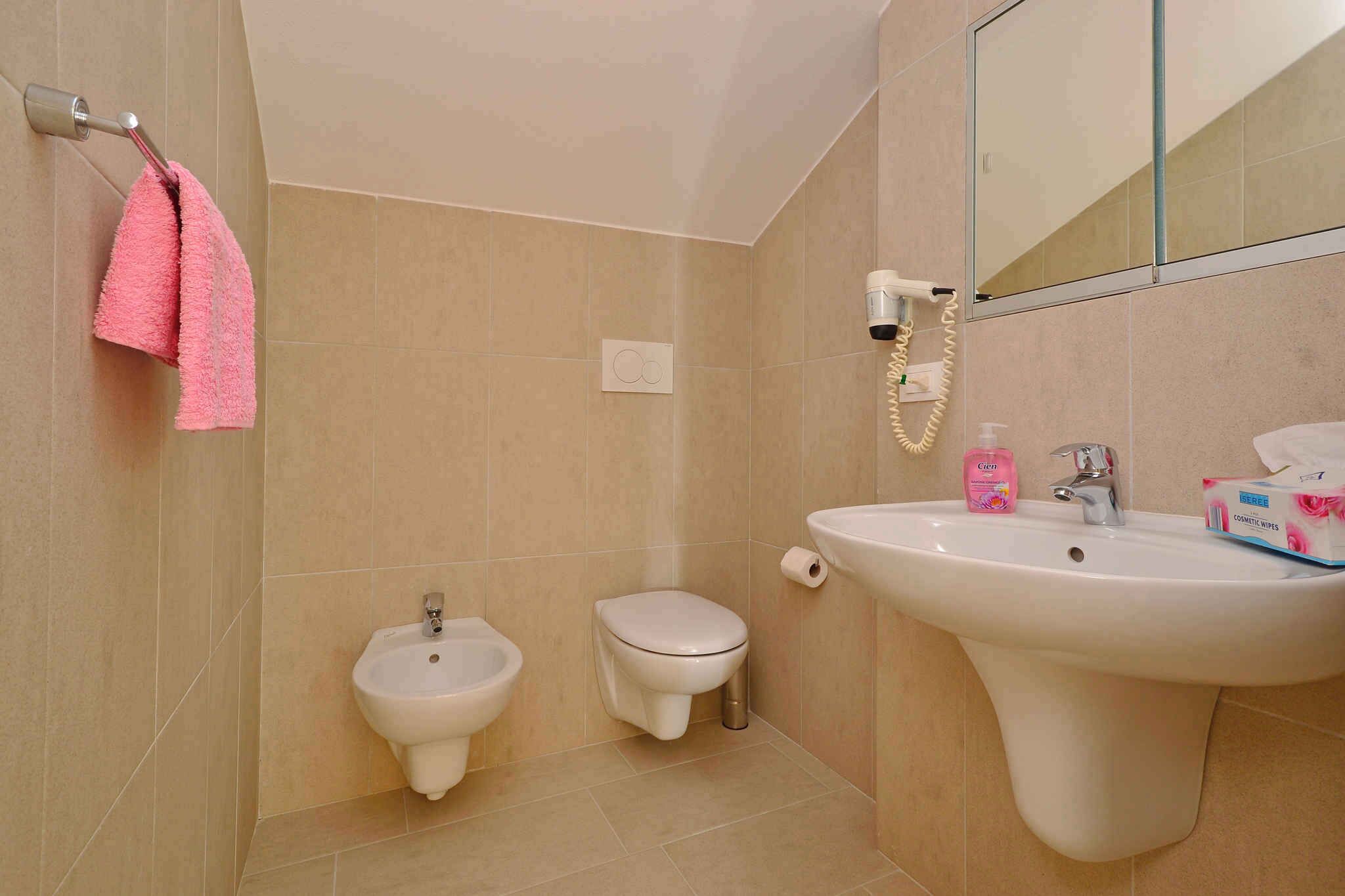 A bathroom with a bidet, toilet, sink, and a towel rack with a pink towel.