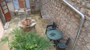 Un muro de piedra, una reja de metal, una mesa redonda con sillas y una butaca de metal.
