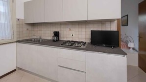 Una cocina moderna con armarios blancos, estufa a gas, cafetera y televisor de pantalla plana.