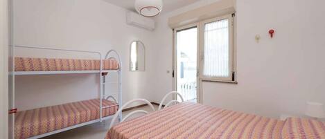 Un dormitorio con literas, una cama individual, una silla, un ventanal y un equipo de aire acondicionado.