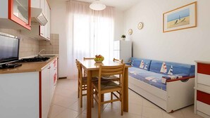 Uma cozinha compacta com mesa e cadeiras, um sofá com tema náutico e uma geladeira pequena.