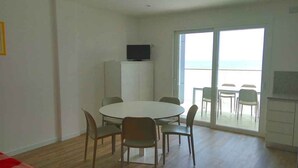 Et værelse med et rundt bord og stole, et fjernsyn på et skab, samt en balkon med siddepladser.