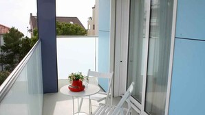 Un balcon avec une table et des chaises blanches, une plante en pot et une porte vitrée.